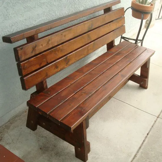 Dark stained timber garden bench with a slatted seat and three-plank backrest against a wall