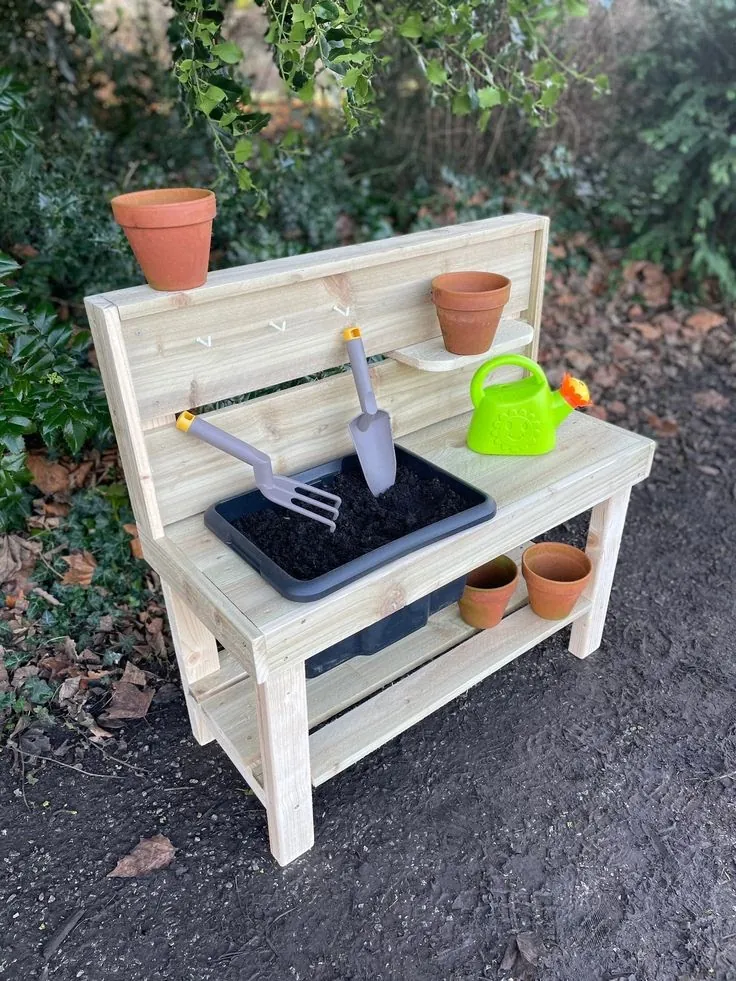 Child-sized pine potting bench with a soil tray, tool hooks, a small shelf and a lower shelf for pots