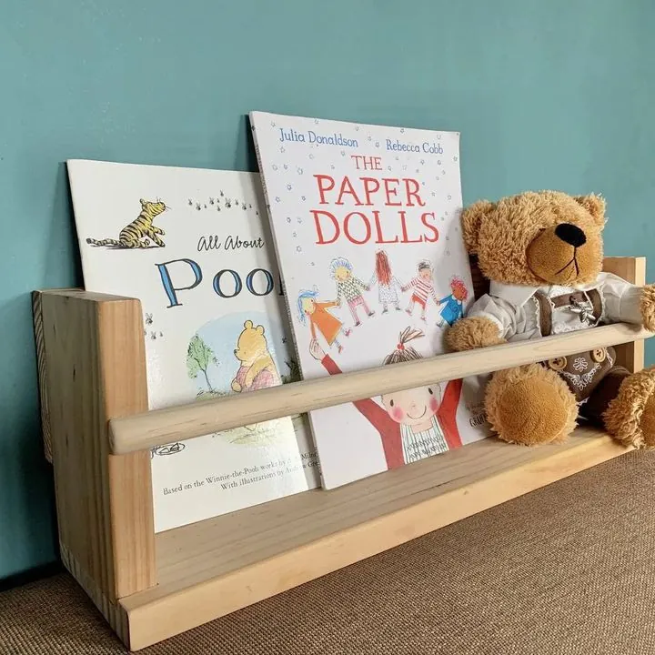 Pine wall book ledge with a round dowel rail holding children's picture books and a teddy