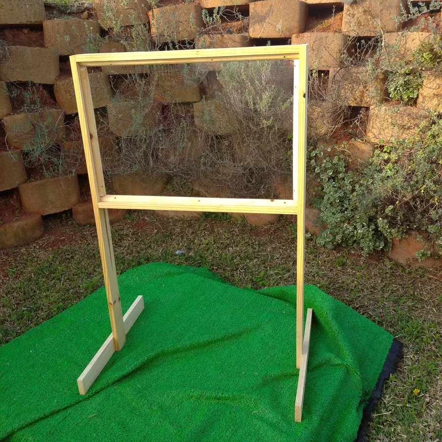 Freestanding pine frame easel with a clear panel and T-shaped feet, set up on artificial grass