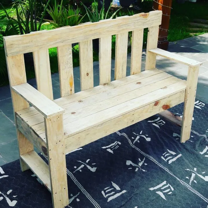 Raw pine garden bench with a slatted back and flat armrests on a patio