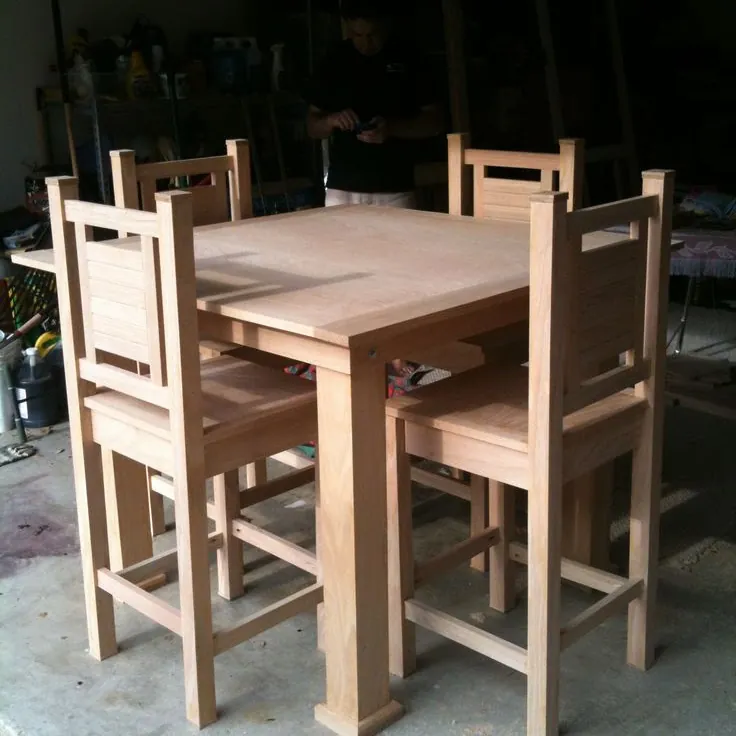 Unfinished square table with four tall slatted-back chairs in a garage