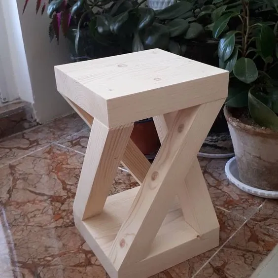 Raw pine side table with a chunky square top and crossed Z-shaped legs on a tiled floor