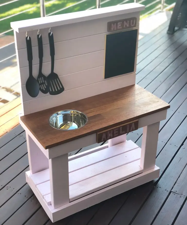 Pale pink and white mud kitchen with a stained top, bowl sink, menu chalkboard and name sign