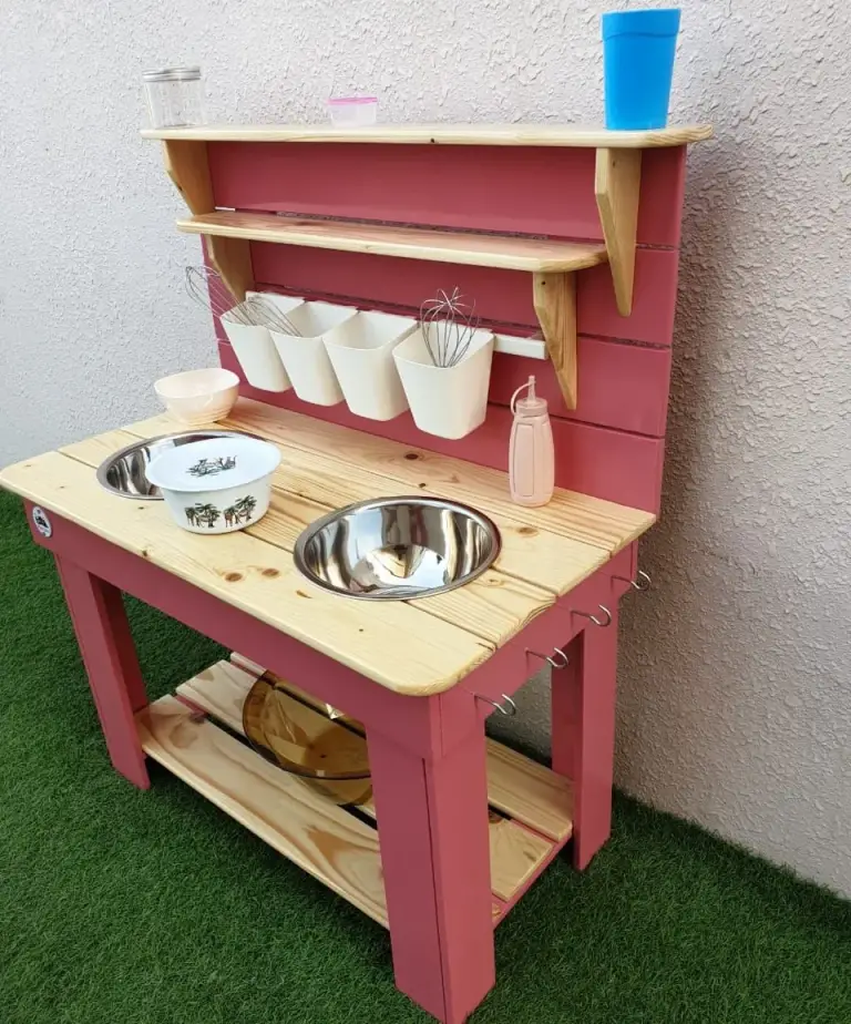 Raspberry-painted mud kitchen with a pine worktop, two bowl sinks, shelves and white utensil holders