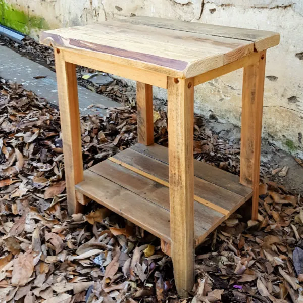 Reclaimed timber side table with a natural-edge top and slatted lower shelf among autumn leaves
