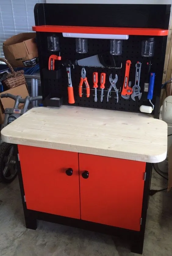 Red and black kids workbench with a pale timber top, black pegboard of toy tools and two cupboard doors