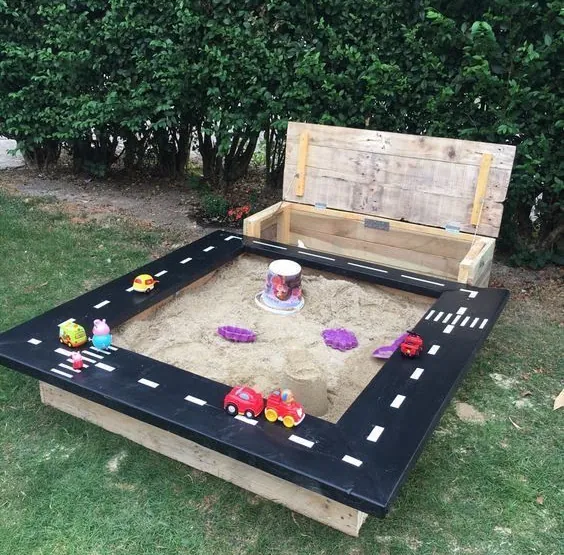 Square sandpit with a black road-track painted rim and a lidded pallet-wood toy box