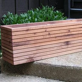 Long trough planter made of thin horizontal hardwood slats with a warm oiled finish