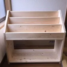 Small unfinished pine book rack with three angled tiers and an open shelf below