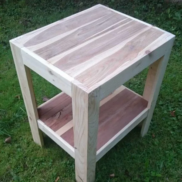 Pale pine side table with pinkish timber top and lower shelf, standing on grass