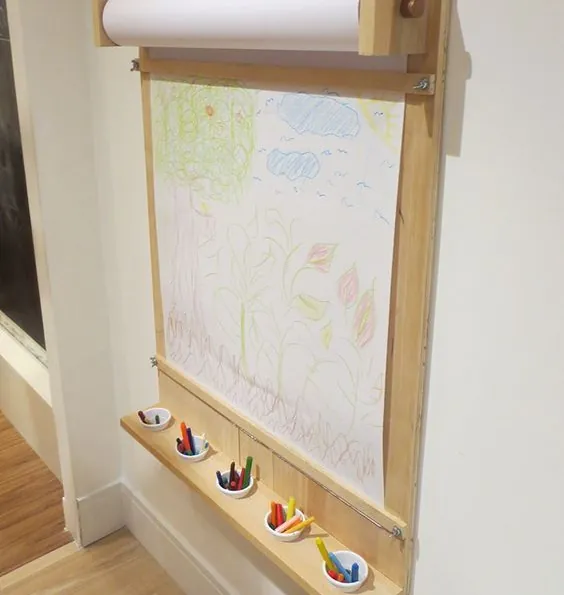 Wall-mounted pine art easel with a paper roll on top and a ledge holding crayon pots