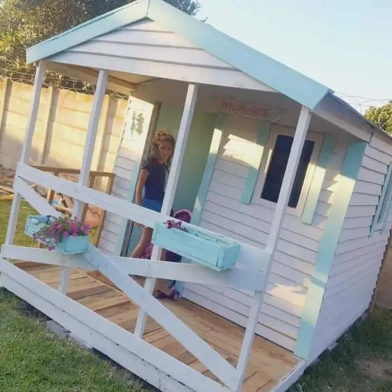 White Wendy house with mint trim, a wide veranda, cross-braced railing and window boxes