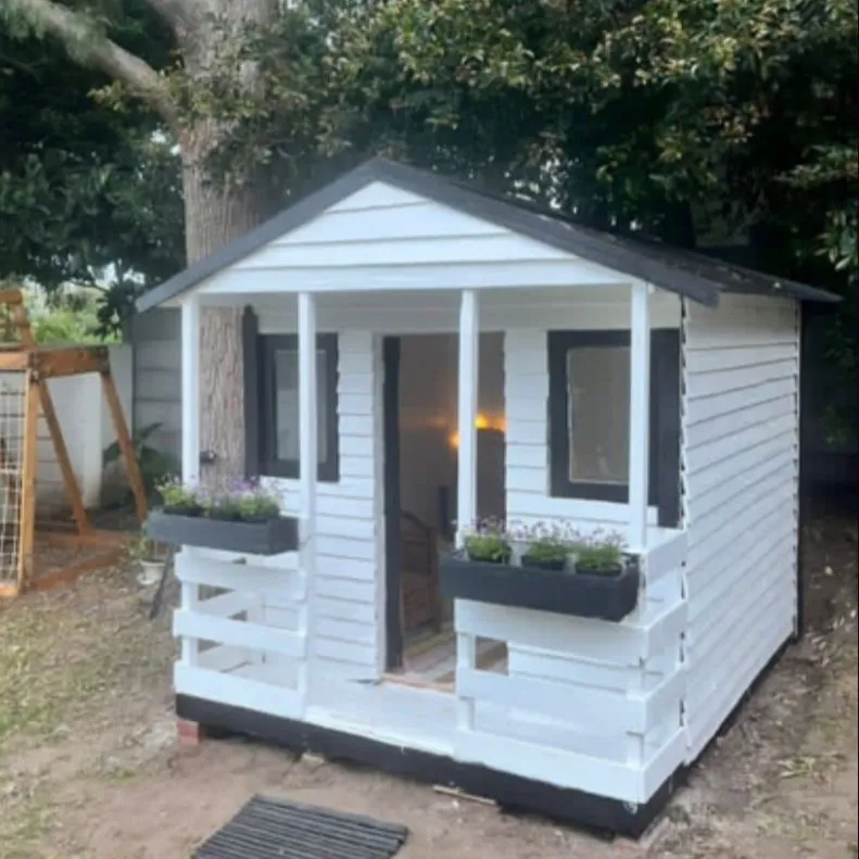 White Wendy house with black trim, covered veranda, window boxes and a pitched dark roof